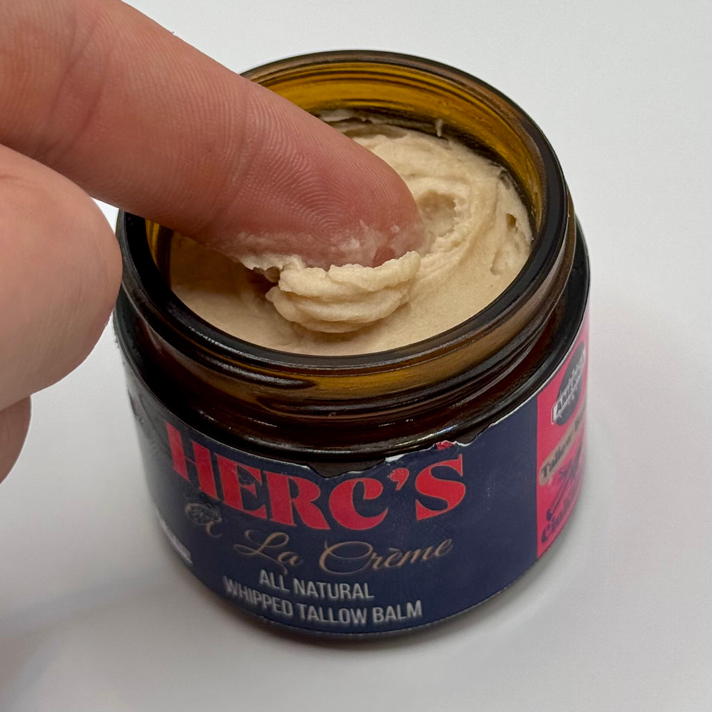 Hand holding a jar of Herc's La Creme whipped tallow balm with visible cream.