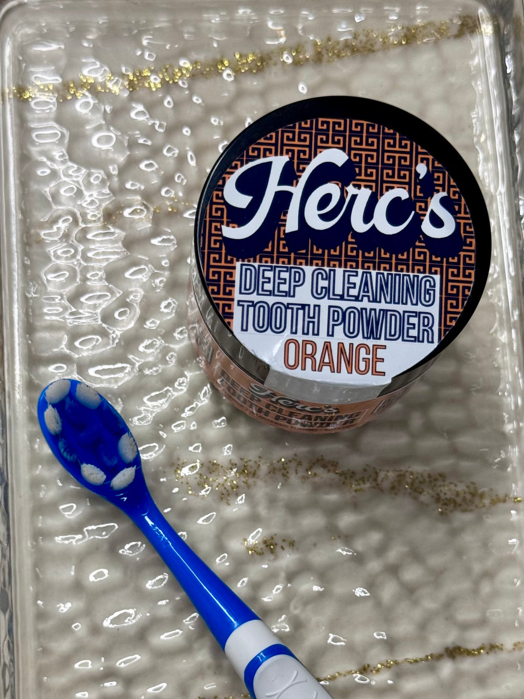 Herc's deep cleaning tooth powder container with a blue toothbrush on a textured surface